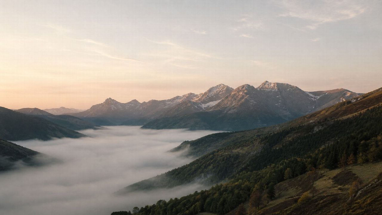 Vista panorámica de un valle de montaña al amanecer, con niebla baja entre las laderas